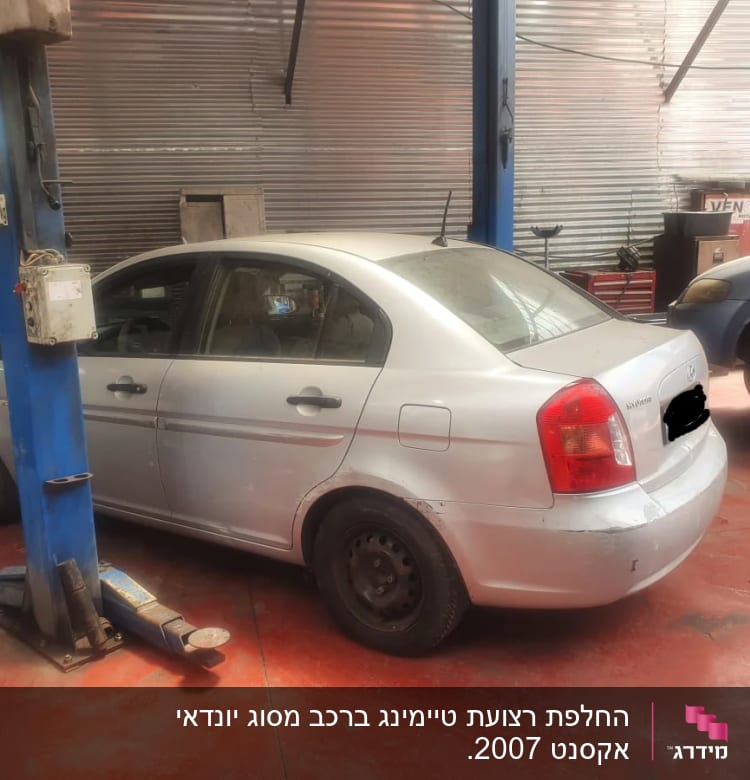 רכב במוסך על רצפת בטון אדומה עם עמודי הרמה כחולים